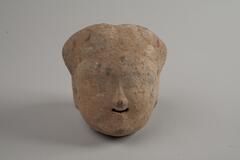 Indian terracotta head figure with most of the facial features being eroded, but the nose and the smiling mouth can still be identified.