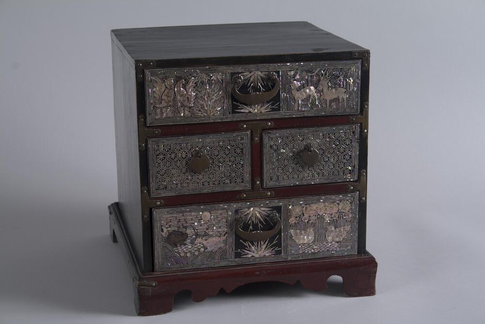This laquer comb chest with mother-of-pearl inlays has images of phoenixes and their babies, and deer on the top drawer, and tortoises and mandarin ducks on the bottom drawer, each in a pair. The handles are in the shape of bats.<br />
<br />
This ornate comb case glitters with the overall decoration of mother-of-pearl inlay. This case was used by women to store toiletries, such as cosmetics, combs, and oiled paper for collecting hair that falls off when combing (<em>toeballang</em>), etc. Four drawers of the case are arranged in three rows. The uppermost tier and lowest tier have one drawer each. These are decorated with auspicious images: mandarin ducks, deer, and turtles. At the second row, two drawers are decorated with hexagon patterns. Techniques such as <em>kkeuneumjil</em> (cutting thin nacre threads and attaching them according to the design) and <em>jureumjil</em> (cutting nacre according to the design with fretsaws, scissors, knives, etc. and attaching the piece to the lacquered surface) were use