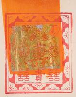 Woodblock print with red floral design framing an inner square that contains six characters in the top and lower right, center, and left corners and a large character (&quot;longevity&quot;) in the middle with an image of two coins suspended from the wings of a stylized bat in the lower center. Swath of orange paint and imitation gold foil in the middle.