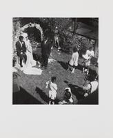 Black and white image of a marriage ceremony with the bride and groom sitting beneath a decorated archway. 