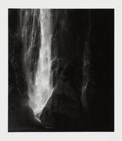 A black and white image of a waterfall. &nbsp;The area is dimly lit, creating a dramatic contrast between the water and its dark surroundings.