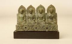 A molded and incised relief sculpture of four seated Buddhas, on a dais with floral rosette motifs.