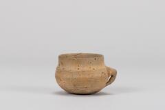 It has a flat base, globular body and straight neck. There was a bubbling of the clay surface during firing. The attached handle is a little small and thick.<br />
<br />
This is a yellowish gray, low-fired earthenware cup with a handle. The mouth is upright, while the rest of the body has a swollen belly and a round base. The handle attached to the lower middle section of the body is not functional. Traces of rotation and water smoothing are visible on the inner and outer surfaces of the mouth.
<p>[Korean Collection, University of Michigan Museum of Art (2017) p. 68]</p>
<br />
&nbsp;