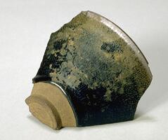 A fragment of a conical bowl on a tall straight foot ring, covered in a dark brown-black glaze with intense and copious russet and ochre hare's fur markings (兔毫盏 <em>tuhao zhan</em>).