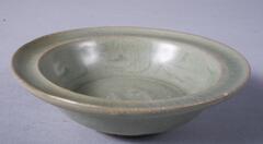 A small stoneware bowl on a foot ring with an everted, concave rim.  The interior is molded with two fish and covered in a gray-green celadon glaze.