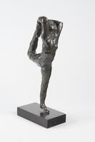 A bronze sculpture of a dancer. The dancer is shown standing on one foot while stretching the other foot to the back of her head.