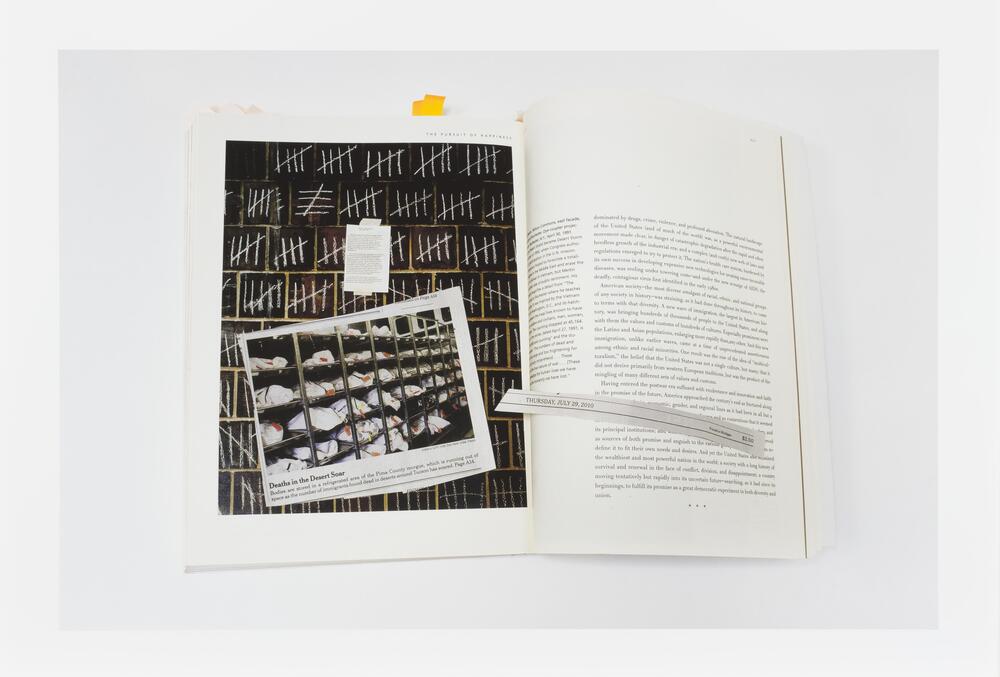 Image of a book lying open to a page featuring an image of tally marks on a wall. A newsclipping featuring a photo of bags on shelves lies on the book across the open page.  