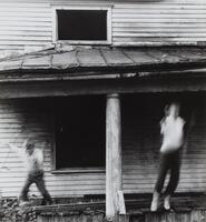 A photograph of two boys jumping off the edge of a porch on a house.