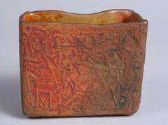 This small square vase has a body with a raised pattern and a matte glaze of orange and brown colors.