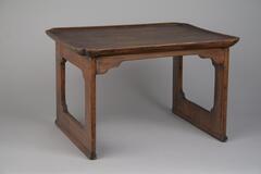 Small wooden table with a beveled table top. The legs consist of two attached pieces of wood with a center square cutout with rounded corners. The design element of rounded edges is reflected in the corners of the table tops.<br />
<br />
This table has a rectangular table top with its brim rounded in four corners. The leg-panels are in a simple form with openwork decoration. Each apron is nailed to the leg-panels on either side. The bottom of each leg-panel is halved and inserted into the stretcher, then fixed with wooden pegs to reinforce the joints.
<p>[Korean Collection, University of Michigan Museum of Art (2017) p. 260]</p>
<br />
&nbsp;