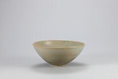 <p>This bowl is an example of an early celadon influenced by Chinese Yue ware. Similar vessels have been excavated from sedimentary layers of the Kiln no. 10 at Yongun-ri, Gangjin-gun, Jeollanam-do. The design, which features two parrots with their wings spread around the bowl&rsquo;s inner wall, is also similar to the design found in Yue ware. This piece counts as medium quality ware, since its glaze is poorly fused. Refractory spurs are stuck around the rim, while the glaze has flowed downwards. There are six refractory spur marks on the shallow foot.<br />
[<em>Korean Collection, University of Michigan Museum of Art</em> (2014) p.90]</p>
Stoneware teabowl with celadon glaze. A pair of parrots is incised on he inside of the bowl, as well as a line that runs slightly below and parallel to the rim.