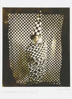 A sepia-toned image of a figure cloaked in a black and white checked fabric, wearing a tall and pointed black and white checked hat, sitting in front of a black and white checked background.