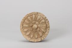 This lotus medallion designed on this round tile-end consists of thirteen petals. The outer rim is decorated with eighteen round dents. The inner ring of the seedpod contains a big central seed surrounded by seven peripheral seeds. The outer rim is embellished with a bead pattern.<br />
<br />
This gray-white, low-fired earthenware tile features a single-tier, thirteen-petal lotus design and is made from fine clay. The large lotus seed at the center of the ovary is surrounded by seven slightly smaller seeds. Evidence of repair using gray clay is visible on the reverse side of the tile.<br />
[Korean Collection, University of Michigan Museum of Art (2017) p.37]