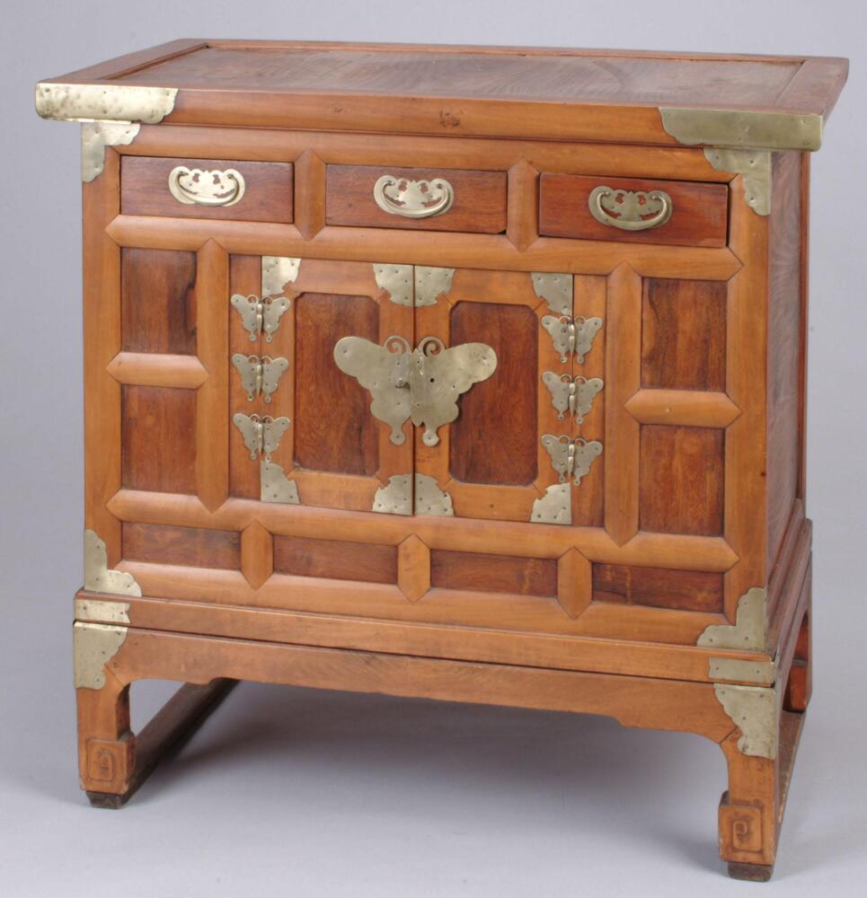 This is a low pear wood storage chest, with three drawers and two doors. The butterfly and bat brass fittings for the hinges and drawer pulls add 'feminine' touches.