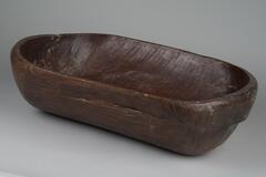 Large oblong, rectangular wooden bowl with rounded ends.<br />
<br />
These large bowls (<em>hamji</em>) were made by carving out large, single pieces of wood. Notches or handles have been carved out on two opposite sides of the outer walls, making them easy to carry. Round hamji bowls were sometimes carved on a turning lathe, but those with notches could be made by carving out single lengths of wood with an adz. These bowls were used in towns and the countryside alike. Affluent households would possess sets of large, medium-sized, and small bowls with notches piled up together. When grinding mung beans, beans, or red beans, such bowls are placed below a grindstone supported by a tripod.
<p>[Korean Collection, University of Michigan Museum of Art (2017) p. 274]</p>
