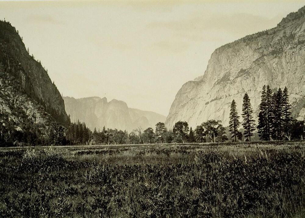 Photographed from ground level, this image depicts a wide view of a valley floor surrounded by tall cliffs on either side.
