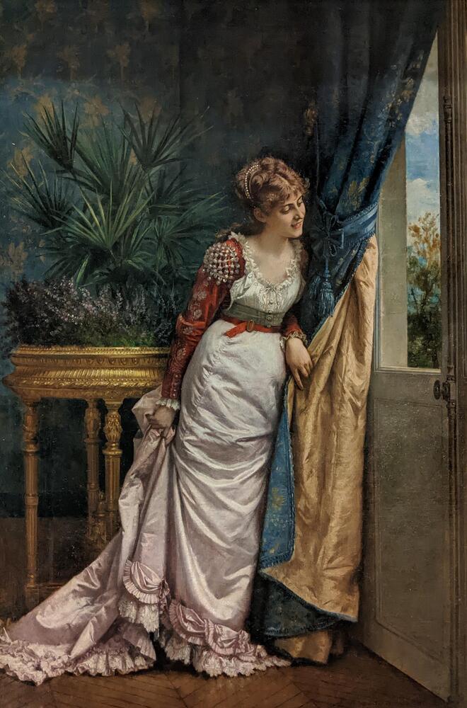 Painting featuring a woman wearing a pink and white dress with a train and bustle pulling back a curtain in front of an open window. The woman is in a room decorated with blue and green wallpaper matching the curtain and she stands in front of a table containing potted plants.&nbsp;