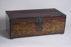 A short, long wooden chest with a papered front. The metal fittings on the chest are vert dark, and the front latch is attached to the chest with a circular piece of metal, and the latch itself is a thin piece of metal placed vertically. A small metal handle is located below this. The wood is a dark red color, and the papered front depicts flowers, with the predominant color being yellow. Orange is also used in some of the flowers, and on the circular shapes spaced along the bottom of the image. The outlines of the flowers and other images are painted in black.<br />
<br />
This chest is papered over wooden frame. It has been repaired following partial damage to the rear hinges, the base, front panel and the paper decoration on the left and the right. The wooden frame is joined by butt joints and not miter joints, following the trend which was popular during the Japanese annexation of the Korean Peninsula. The box is therefore assumed to have been produced at this time, then repaired later. None of its orig