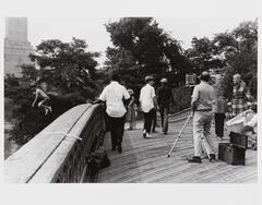 A young boy jumps off a bridge, while a fashion photography shoot is staged on the bridge.