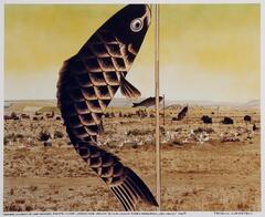 This photograph depicts a view of a desert landscape with a fish hanging from the top of a thin pole in the foreground. &nbsp;Behind the fish is a small cemetery that has mounds and crosses and in the distance are a few small buildings. Two more poles with fish hanging from them appear farther away in the image to the right of the fish in the foreground.