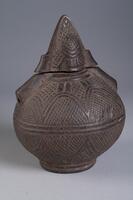Globular container with circular base and cone-shaped lid. There are two tunnel-like holes symmetrically opposing, another vertically traveling through the lid down the sides of the container. Large looping circular patterns with small diamond grids are carved across the entire container.