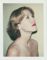 A portrait of a woman; her torso turned toward the right side of the frame. She looks up, tilting her head back. She wears white makeup and red lipstick to flatten her features for a future offset lithograph. 