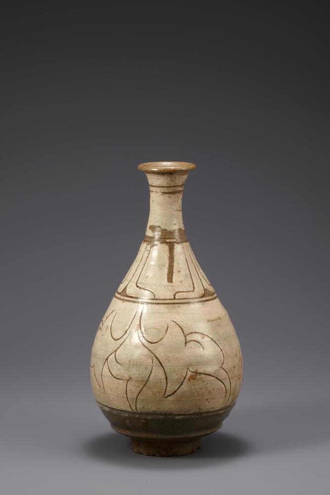 Pear-shaped stoneware wine bottle with white slip and sgraffito designs. Stylized foliage is incised across the main register of the body, separated from the register above by two incised bands. Above this are perhaps incised stylized petals, and separating them from the flared lip of the bottle are two more incised bands. The incisions reveal the gray clay beneath the white slip.<br />
<br />
<br />
This bottle is painted with thick white slip on its entire body and lotus petals decorate below the neck using a sgraffito technique. With a sharp tool, white slip is carved away from the belly to form scrolls. Traces of fine grains of sand remain on the rim of the foot, while the outer base also retains the marks of an implement that is pressed again the base. These are common characteristics shared with other pieces of 15th and 16th century buncheong wares. The glaze is well fused, producing a shiny surface, pale green and transparent.<br />
[Korean Collection, University of Michigan Museum of Art (2014) p.