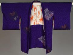 Purple silk damask (rinzu) in T-paper pattern (sayagata), bokashi dyed so that the shoulders are a darker purple than the lower half of the haori.  Woven designs of phoenixes, paulownia, cranes, chysanthemums, etc., incorporate metallic threads.  Lining is orange and white silk.  There are purple and white kumihimo (a kind of cord) with tassels.