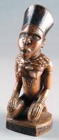 Kneeling female figure with hands placed on knees. The chest and back show scarifications. The teeth are filed and the figure has a flat, raised coiffure. 