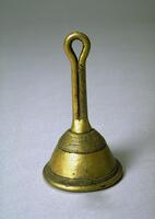 Hand-held bell with a short handle ending in a loop. One side of the handle has a design of incised, diagonal lines. The top of the bell is decorated with horizontal grooves and the bottom edge is decorated with a grid-like design. 