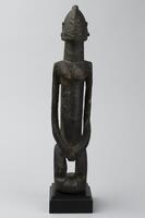 Standing figure with bent knees and its hands at the front of its hips. The head is triangular with protruding u-shaped ears and a ridge extending from its forehead, over the head, and down the back of the neck.&nbsp;