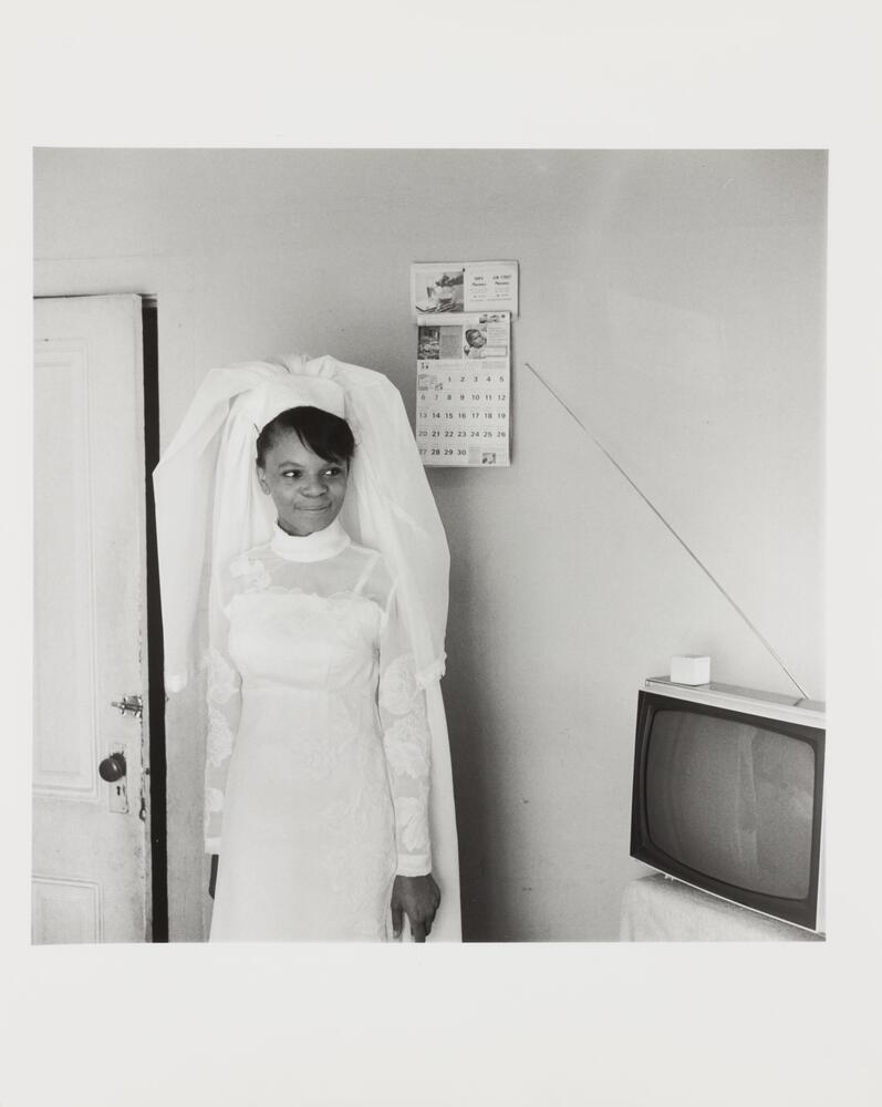 Black and white image of a woman wearing a long-sleeved wedding dress and veil looking to her left.