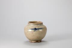 This is a grayish brown small jar with a short neck and a globular body. It is dated to the end of the 19th century, judging from its motifs, color of cobalt-blue and shape. It is decorated with a line around the rim and with floral scrolls on the shoulder. The entire foot is glazed and has grains of coarse sand stuck to it. Extensive contamination from impurities on its surface has given it a yellow tint overall.<br />
[Korean Collection, University of Michigan Museum of Art (2014) p.174]