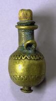 A cast brass container with a round body and a short neck. At the bottom of the container is a knob-like projection. The body of the container is decorated with incised lines and raised, undulating lines around the top and bottom edge. Near the neck is a small loop. The top of the container is closed with a wooden stopper. 