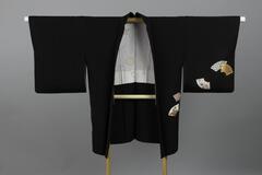 <p>Black formal chirimen haori with colorful dyed, patched, and interwoven folding fan motifs on the left front and back sleeves and on the lower back and front with a silk white inner lining with hand-painted pale floral designs. It has one family crest on the center on back.</p>
