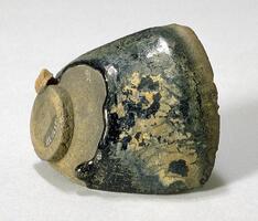 A fragment of a conical bowl on a tall straight foot ring, covered in a dark brown-black glaze with intense and copious russet and ochre hare's fur markings (兔毫盏 <em>tuhao zhan</em>) and mottling.
