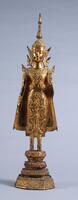 Standing gilt bronze Shakyamuni Buddha with glass inlay.  One hand is raised in the form of the "fear not" mudra.  Stands on a pedestal in ornamented dress and crown.