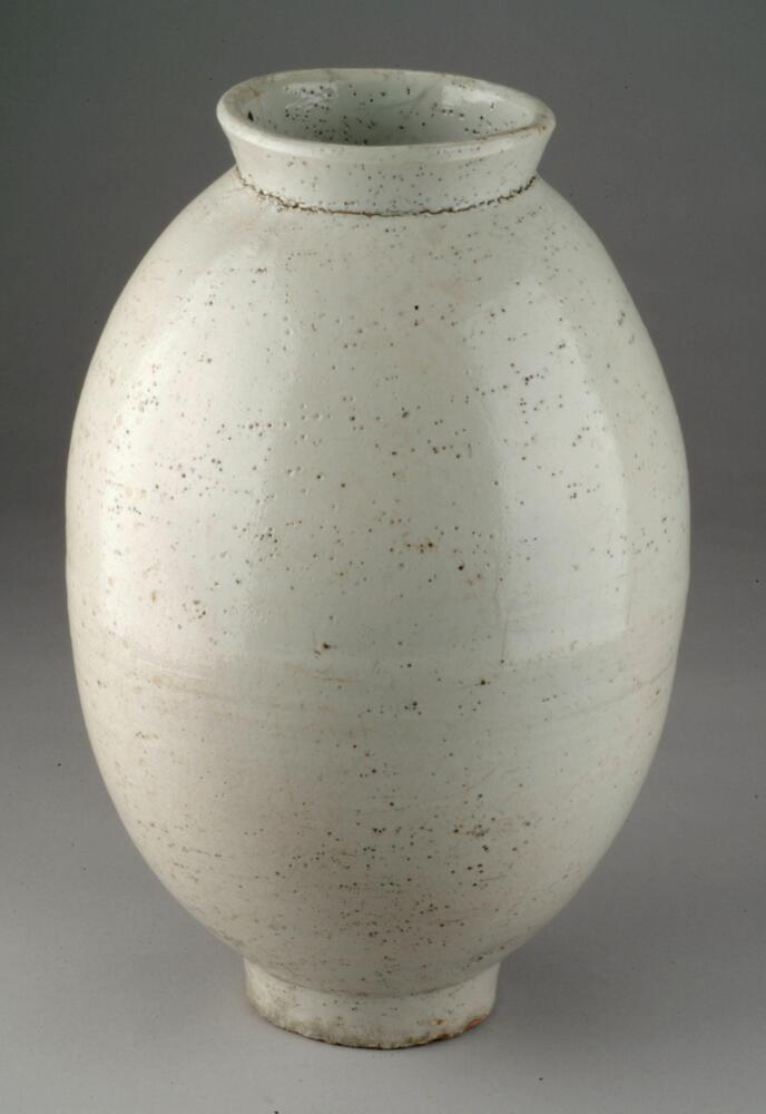 Large porcelain jar with course ovoid body, cylindrical foot, flared mouth and colorless glaze.<br />
<br />
This elongated ovoid jar is presumed to have been produced at a regional kiln. It is shaped by joining the upper and lower halves, which were made separately on the wheel. High-quality clay and glaze were used, but the glaze was poorly fused. The foot was repaired after a partial damage. The lower body features red spots on some parts, which occurred during firing.<br />
[Korean Collection, University of Michigan Museum of Art (2014) p.170]