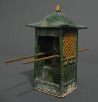 An earthenware, green glazed sedan chair, square with four sides and a hipped roof. It has gold pointed finial, amber latice windows on the right and left, and an open front with a chair. Two poles run horizontally through the sedan chair for carrying by five male attendants (2008/2.276).  