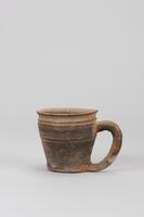 Dark gray high-fired handled cup. Rim is splayed due to strong rotation and water smoothing. Two incised horizontal lines have created a ridge belwo the rim, an effect that is repeated on the upper part of the body of the cup. The loop-shaped handle was attached by piercing the side, causing slight warping.<br />
<br />
This is a dark gray, high-fired handled cup. The rim of the cup is slightly splayed due to strong rotation and water smoothing. Two incised horizontal lines have created a ridge below the rim; this effect is repeated on the upper part of the body. The loop-shaped handle was attached to the body by piercing its side, as a result of which the rim is slightly warped. The base is flat and wide but slightly indented around its edges.
<p>[Korean Collection, University of Michigan Museum of Art (2017) p. 68]</p>
