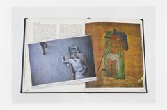 Image of a book lying open to a page featuring a painting of the crucified Christ. A newsclipping featuring a photo of an ash-covered body of a man lies on the book across the open page.  