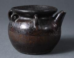 Black ceramic jar with a spout and a series of loops around the neck through which a cord could be threaded to secure a cover; decorated around the middle with a geometric pattern and striations.