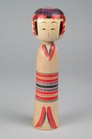 A wooden doll with two tiers made up of a head and body with no arms, legs or feet. Painted on the head is a face, hair, a red and purple headdress. The body is painted to look like it is wearing a tan kimono with red, black and purple stripes in the middle for the obi. You can see where the kimono begins and ends at the top and bottom of the body.