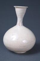 The form of this bottle is unusual in that its body and neck are almost the same length. The glaze is partially oxidized, producing an orange tint, while the surface shows contamination by impurities and pinholes, and cracks are formed towards the foot. The bottle is glossy overall, but the glaze was unevenly applied and has run in some parts. The clay has a high kaolin content, and the bottle has thin, light walls. White porcelain of this kind was produced in Yanggu-gun, Gangwon-do, and Cheongsong-gun, Gyeongsangbuk-do.<br />
[Korean Collection, University of Michigan Museum of Art (2014) p.206]