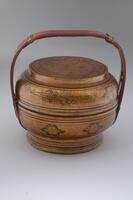 A wooden basket with a lid covered in lacquer gold and floral designs. It has a curved handle.