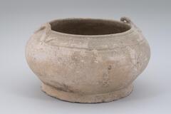 A squat, globular jar with an inverted direct rim. &nbsp;There are two opposing applied coil handles on the rim and a wide footing. It is covered in a pale gray-green celadon glaze.