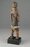 This standing female <em>nkisi mihasi</em>, or “benevolent” power figure, exhibits many of the typical traits associated with the Luba of the Upemba Basin, and more specifically, with the Kisale center of production. These features include a disproportionately elongated torso, terraced coiffure, diamond-shaped scarification patterns covering the abdomen and back, and, a crescent moon symbol on the pubis. In addition, this figure possesses a round head with almond-shaped eyes, an open mouth, flat and level shoulders, protruding breasts and bellybutton, and horizontal lines across its upper thighs. Multiple strands of white, dark blue, and light blue beads adorn the figure’s neck, upper chest, wrist, hips, and ankle. A cotton loincloth has been wrapped around the figure’s hips.