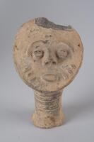 This work is a terracotta head with a narrow, striated neck. The head is flat and circular, slightly tilted back on the neck. The mouth is open with three diagonal marks on each cheek. The eyebrows are formed by one continuous, curved line above the eyes and nose. 