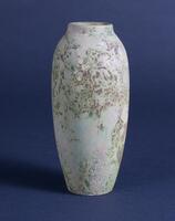 This slender vase has a matte glaze with accents of green, pink and purple in an overall whiteish body.
