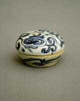 A small porcelain box with the base and the lid similar in size and shape, being round and shallow with curved sides.  The base is on a foot ring, painted with underglaze cobalt blue to depict <em>ruyi </em>(as you wish)<em> lingzhi </em>mushroom-shaped clouds and meander.  It is covered in a clear glaze.